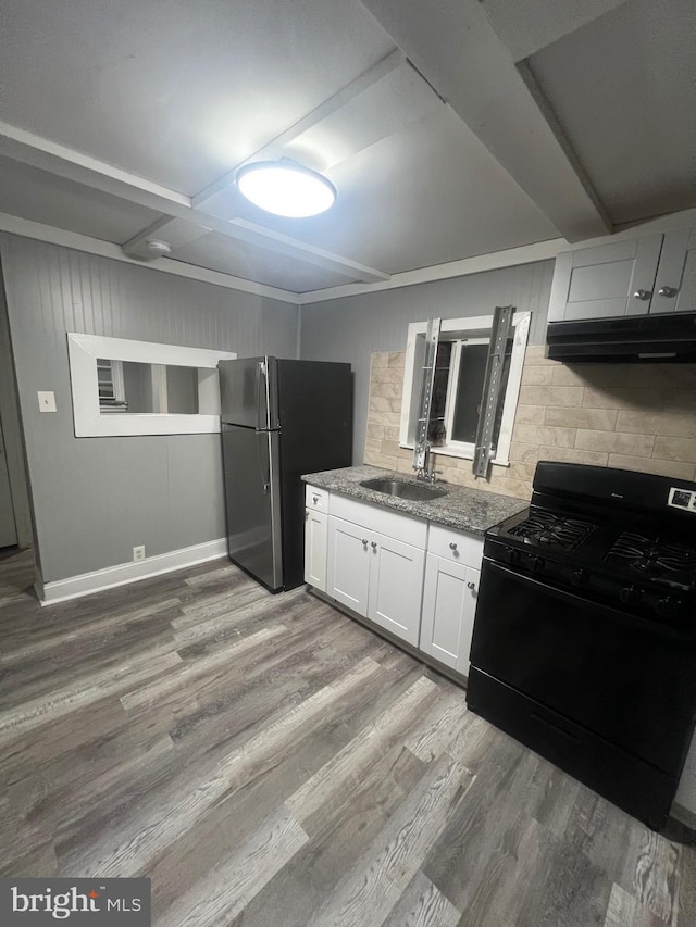 kitchen featuring black range with gas stovetop, sink, range hood, white cabinetry, and stainless steel refrigerator