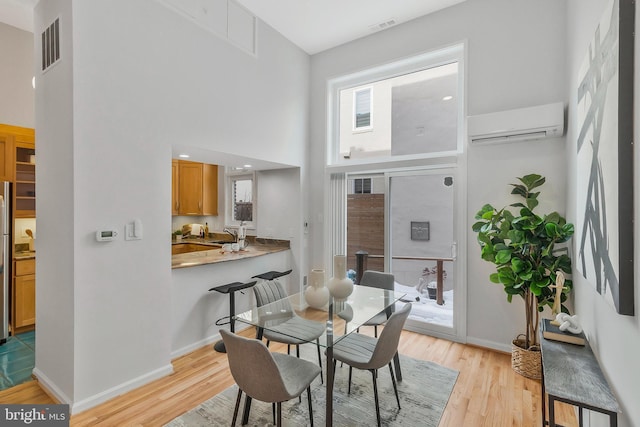 dining room featuring a high ceiling, light hardwood / wood-style floors, and a wall mounted air conditioner