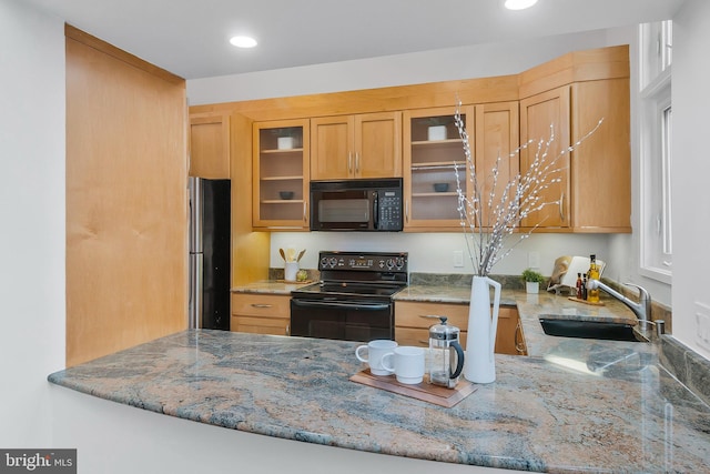 kitchen with light stone counters, kitchen peninsula, black appliances, and sink