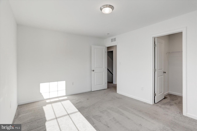 unfurnished bedroom with a spacious closet, a closet, and light carpet