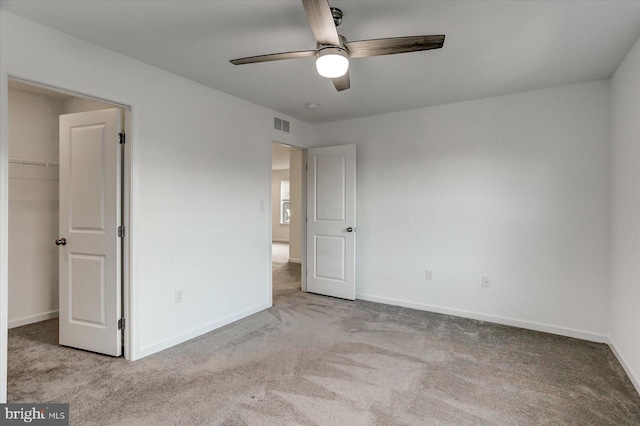 unfurnished bedroom featuring a closet, a walk in closet, light colored carpet, and ceiling fan