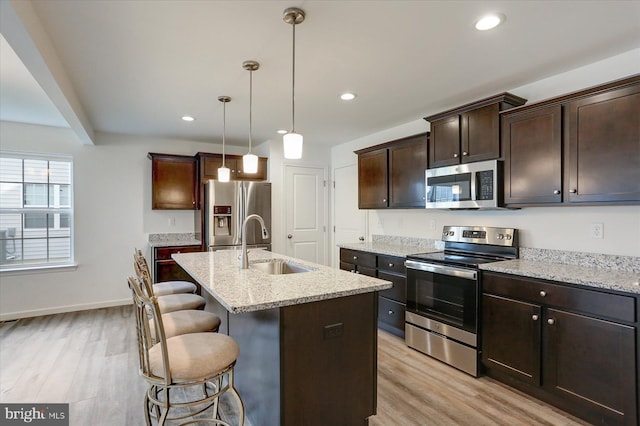 kitchen with a center island with sink, a breakfast bar area, decorative light fixtures, light stone counters, and stainless steel appliances