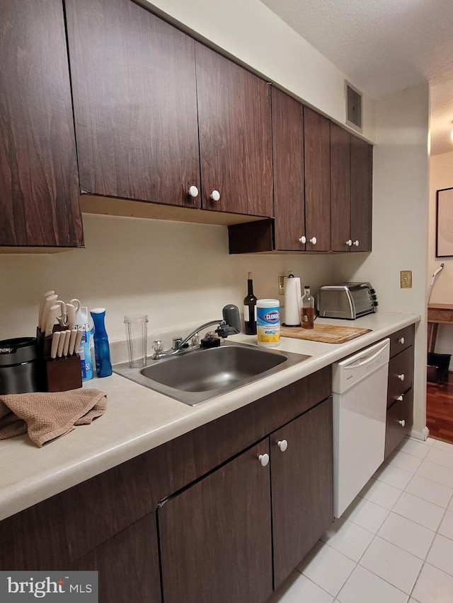 kitchen with light tile patterned floors, white dishwasher, dark brown cabinetry, and sink