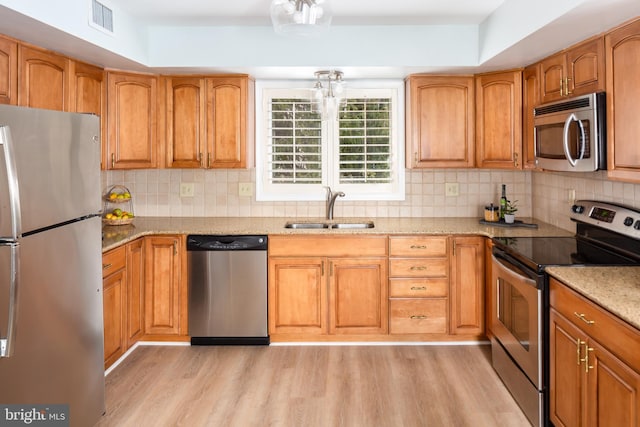 kitchen featuring stainless steel appliances, decorative backsplash, light hardwood / wood-style flooring, light stone counters, and sink