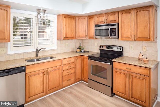 kitchen featuring backsplash, sink, light hardwood / wood-style flooring, appliances with stainless steel finishes, and light stone counters