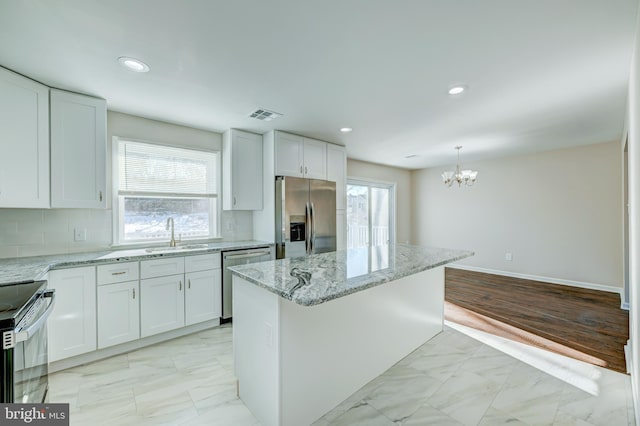 kitchen featuring white cabinets, stainless steel appliances, decorative backsplash, a kitchen island, and sink