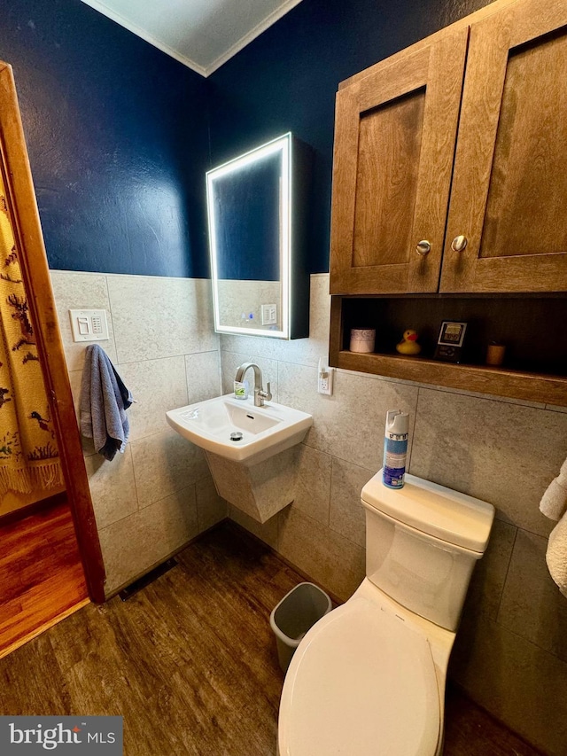 bathroom featuring hardwood / wood-style floors, toilet, ornamental molding, and tile walls