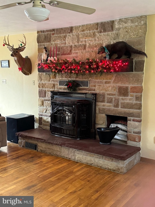 interior details with ceiling fan, a wood stove, and hardwood / wood-style floors