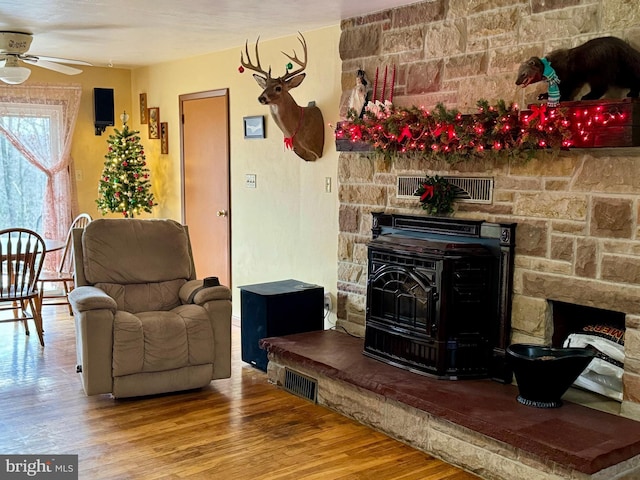 living room featuring hardwood / wood-style flooring, a wood stove, and ceiling fan