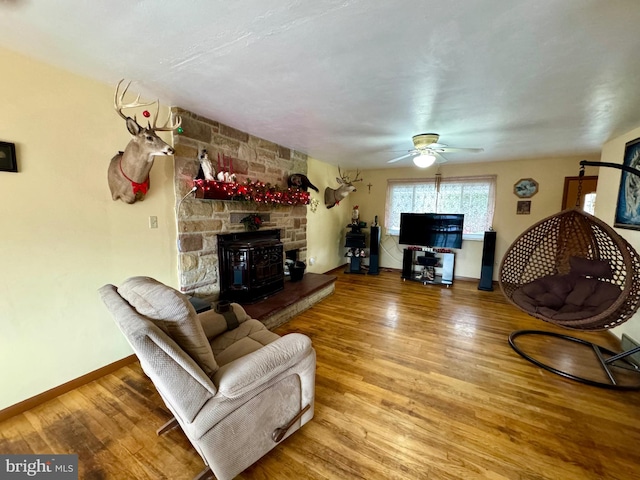 living room with ceiling fan, a wood stove, and hardwood / wood-style flooring