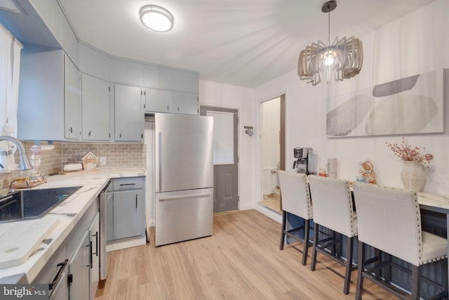 kitchen featuring decorative backsplash, stainless steel appliances, sink, pendant lighting, and light hardwood / wood-style floors