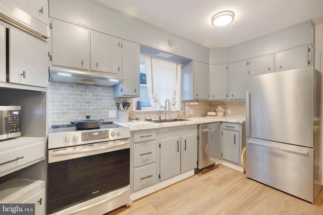 kitchen with appliances with stainless steel finishes, tasteful backsplash, light hardwood / wood-style flooring, and sink