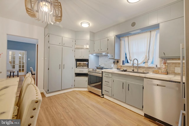 kitchen featuring sink, stainless steel appliances, backsplash, light hardwood / wood-style floors, and decorative light fixtures