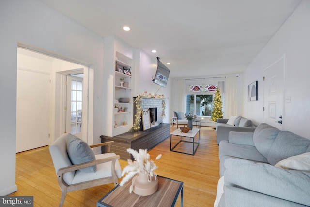 living room featuring built in shelves, a fireplace, and light hardwood / wood-style flooring