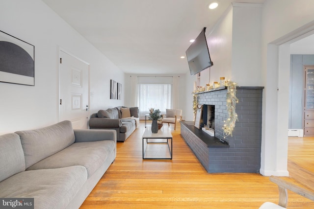 living room with light hardwood / wood-style floors, baseboard heating, and a brick fireplace