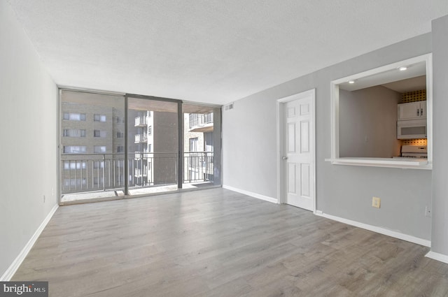 spare room featuring expansive windows, hardwood / wood-style floors, and a textured ceiling