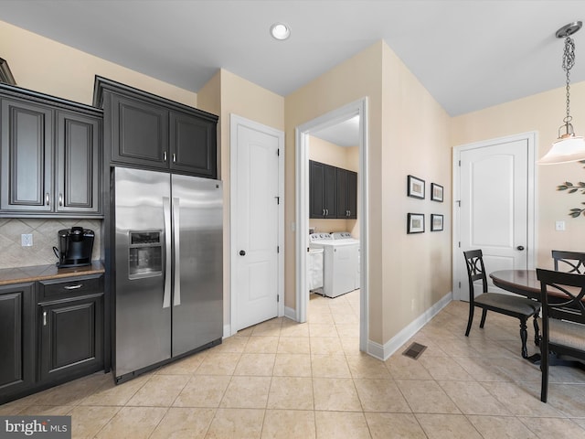 kitchen featuring hanging light fixtures, washing machine and dryer, stainless steel fridge with ice dispenser, decorative backsplash, and light tile patterned flooring