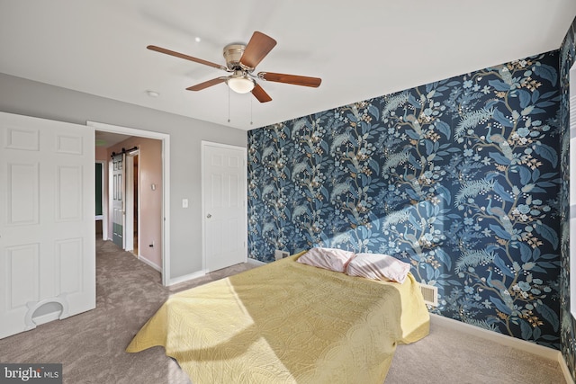 carpeted bedroom with a barn door and ceiling fan