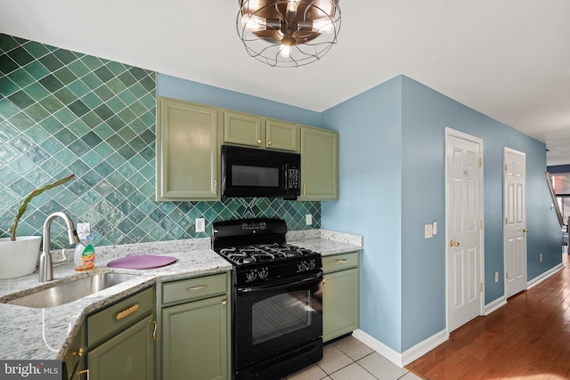 kitchen with sink, green cabinets, light stone counters, decorative backsplash, and black appliances