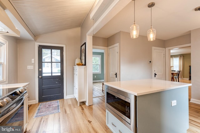 kitchen with lofted ceiling, hanging light fixtures, light wood-type flooring, appliances with stainless steel finishes, and a kitchen island