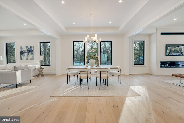 dining area with a notable chandelier, a raised ceiling, and light hardwood / wood-style floors