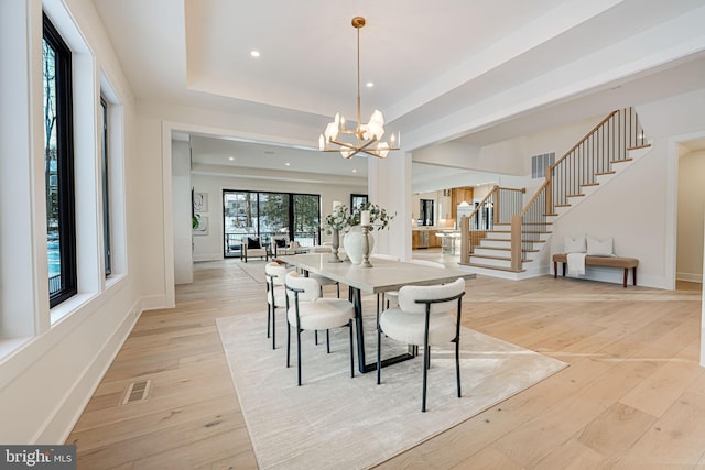 dining space with a raised ceiling, a chandelier, light hardwood / wood-style flooring, and a healthy amount of sunlight