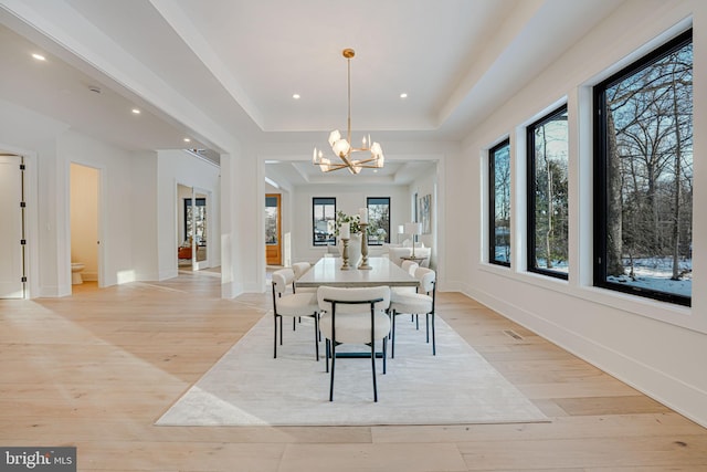 dining room with light wood-type flooring, an inviting chandelier, and a raised ceiling