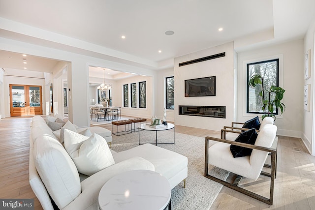 living room with light wood-type flooring, a chandelier, a raised ceiling, and a fireplace