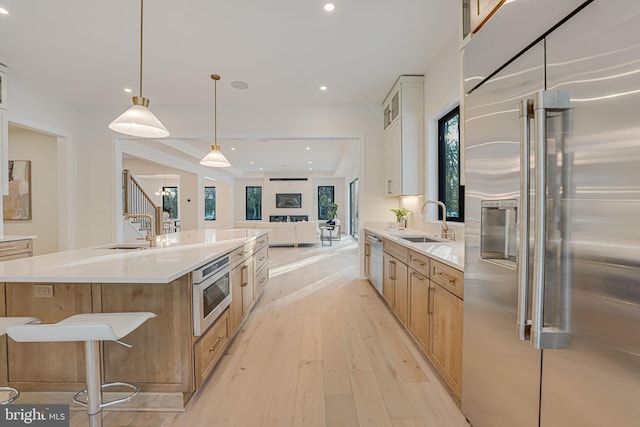 kitchen with a large island with sink, built in appliances, white cabinets, and sink