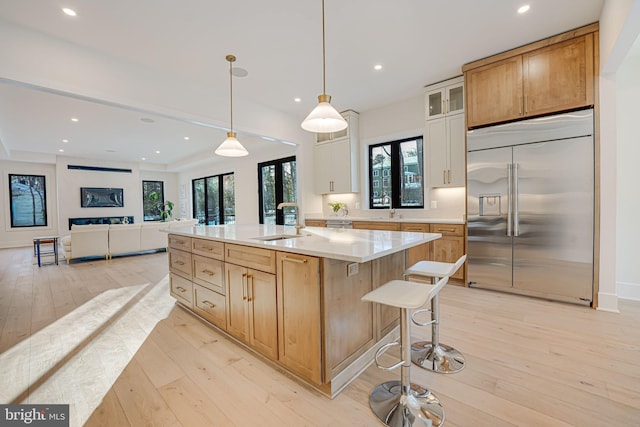 kitchen featuring stainless steel built in fridge, light wood-type flooring, a kitchen island with sink, white cabinetry, and sink