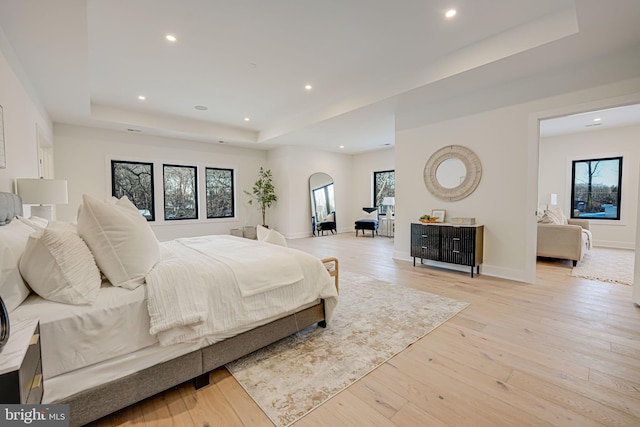 bedroom with light hardwood / wood-style floors and a tray ceiling