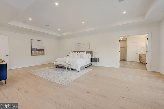 bedroom featuring a raised ceiling, connected bathroom, and light hardwood / wood-style floors