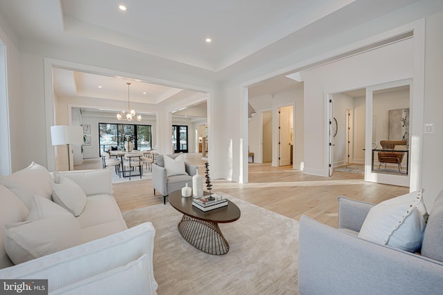 living room with light hardwood / wood-style floors, a notable chandelier, and a raised ceiling