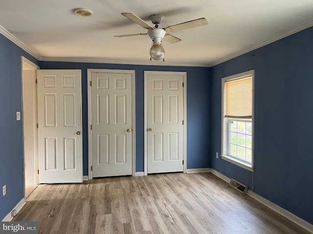 unfurnished bedroom featuring ceiling fan, light wood-type flooring, ornamental molding, and two closets