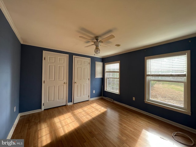 unfurnished bedroom with crown molding, light hardwood / wood-style flooring, ceiling fan, and two closets