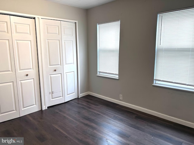 unfurnished bedroom featuring dark hardwood / wood-style flooring, multiple windows, and multiple closets