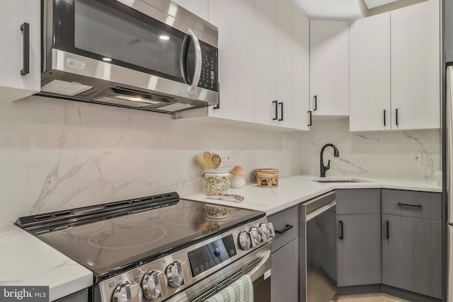 kitchen with light stone counters, gray cabinetry, white cabinets, appliances with stainless steel finishes, and sink