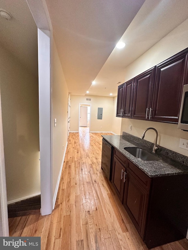 kitchen with light wood-type flooring, dark brown cabinets, sink, dark stone countertops, and electric panel