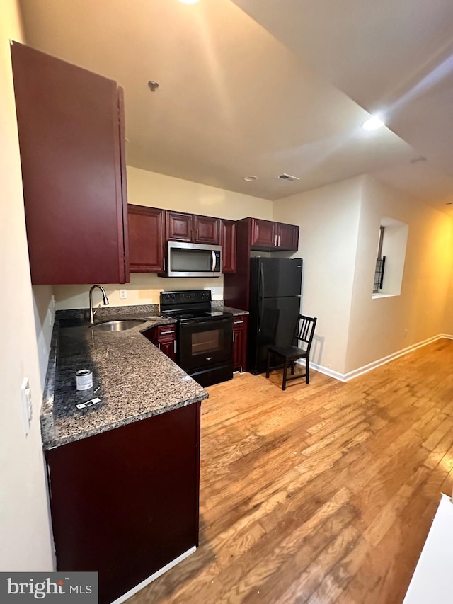 kitchen with sink, light hardwood / wood-style flooring, dark stone countertops, and black appliances