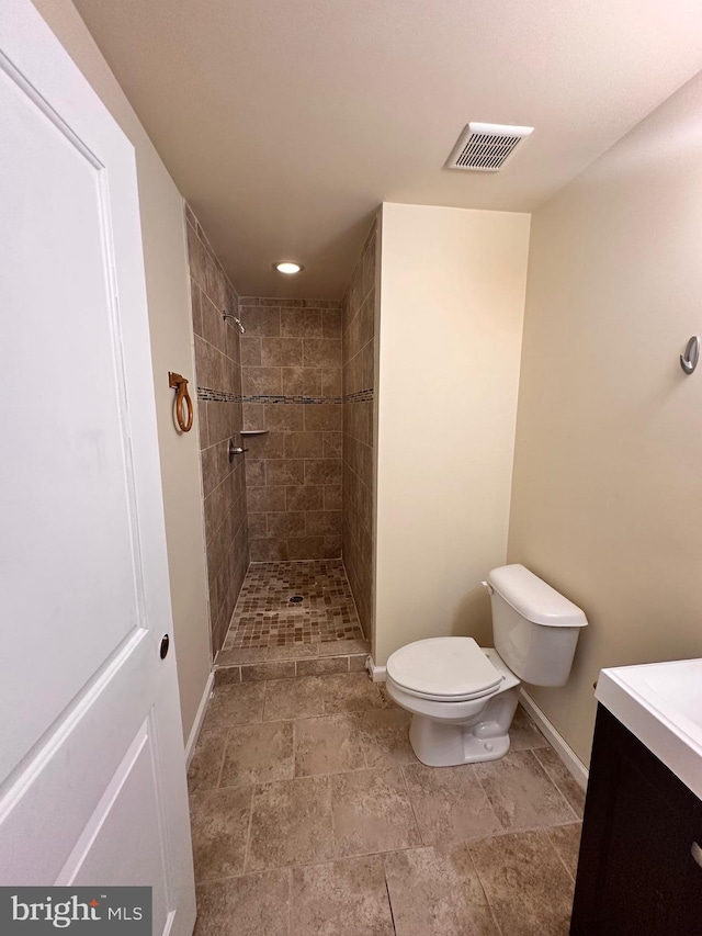 bathroom featuring toilet, a tile shower, and vanity