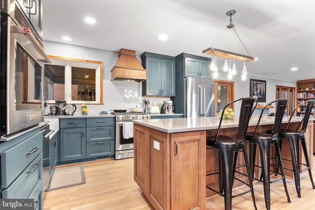 kitchen featuring appliances with stainless steel finishes, custom range hood, decorative light fixtures, light hardwood / wood-style flooring, and a kitchen island