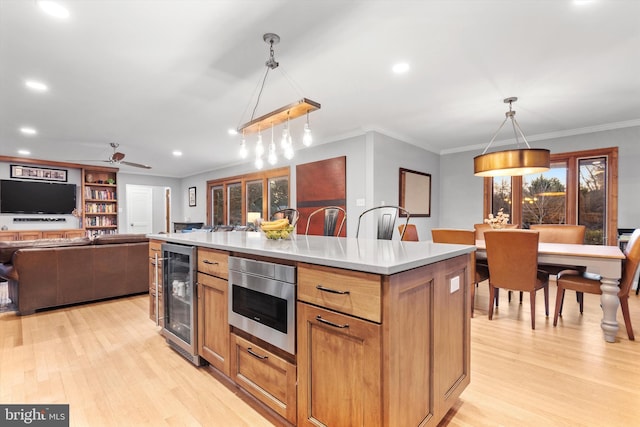 kitchen with ceiling fan, a center island, beverage cooler, hanging light fixtures, and light hardwood / wood-style flooring