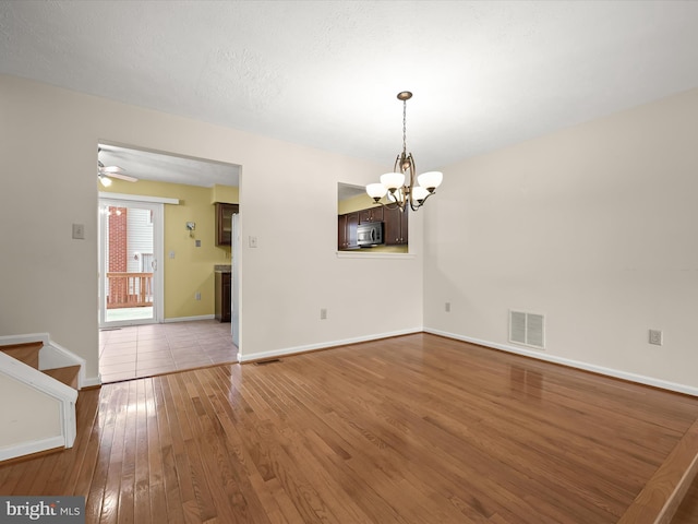 unfurnished dining area featuring ceiling fan with notable chandelier, a textured ceiling, and wood-type flooring