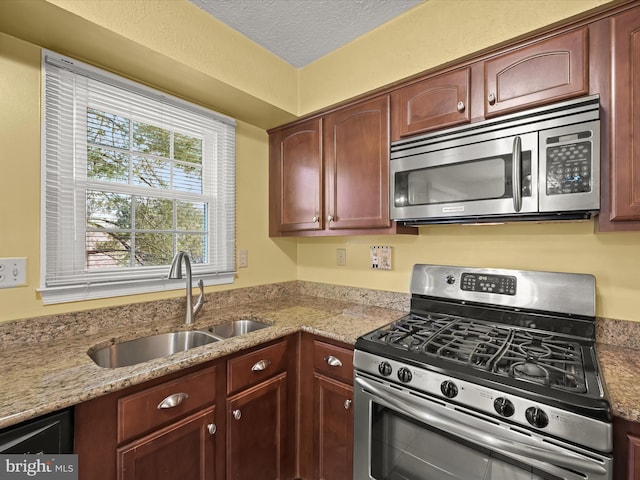 kitchen with sink, a textured ceiling, light stone countertops, and stainless steel appliances