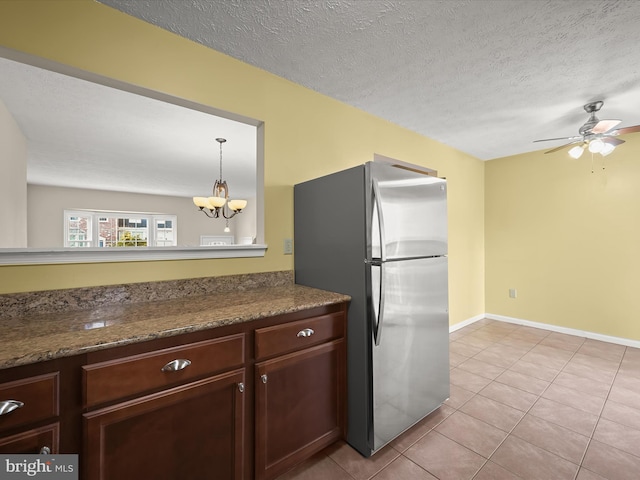 kitchen featuring stainless steel fridge, decorative light fixtures, dark stone counters, light tile patterned flooring, and a textured ceiling