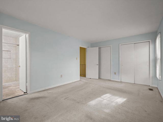 unfurnished bedroom with multiple closets, light carpet, and ensuite bath