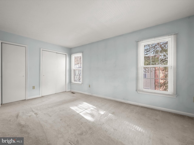 unfurnished bedroom featuring light carpet and two closets