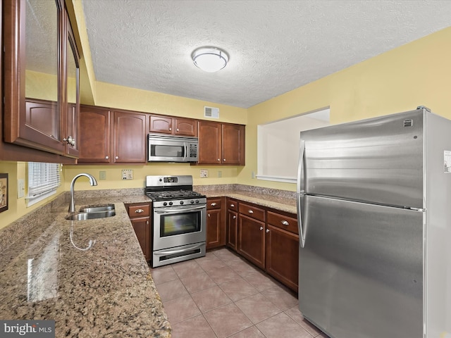 kitchen with a textured ceiling, light tile patterned floors, sink, stainless steel appliances, and light stone counters