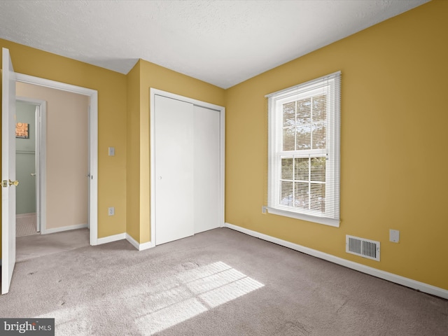 unfurnished bedroom with a closet, a textured ceiling, and light carpet