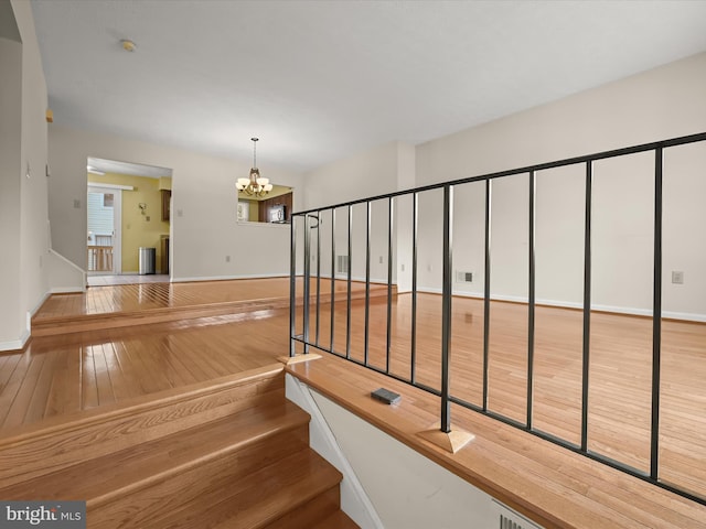 stairway with hardwood / wood-style floors and a notable chandelier